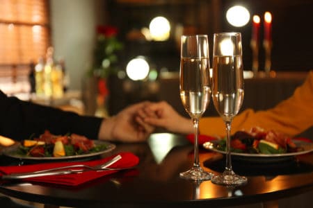 Couple having romantic dinner in restaurant, closeup. Focus on glasses of champagne