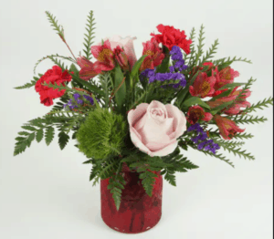 A beautiful traditional arrangement with pink roses, red carnations, trick dianthus, alstromaria accented by purple statice and lush greens in a colored glass vase.